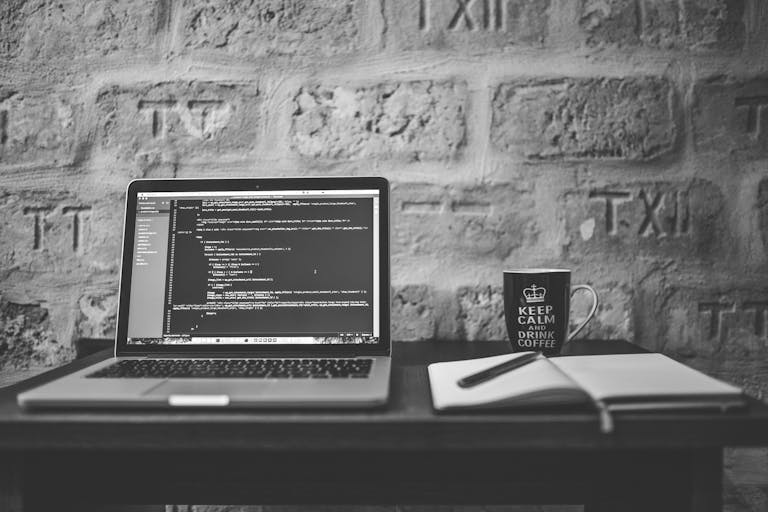 Photo en noir et blanc d'un espace de travail de codage avec un ordinateur portable, une tasse et un cahier.
Développement d'une application web en cours