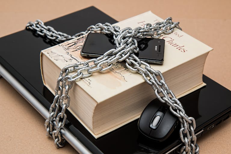 Livre, téléphone et ordinateur portable enchaînés symbolisant la sécurité numérique et intellectuelle. Cela représente bien la sous-traitance en marque blanche