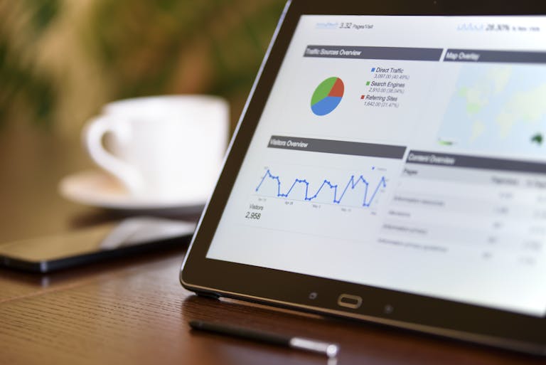 Gros plan d'une tablette affichant des graphiques d'analyse sur un bureau en bois, à côté d'un smartphone et d'une tasse à café. étude des statistique SEO